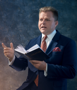 A person in a suit reading a bookDescription automatically generated with medium confidence