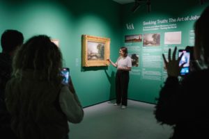 A person pointing at a painting on a green wallDescription automatically generated with low confidence