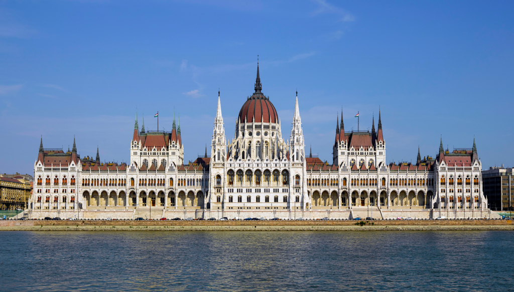 A large white building with a dome and towers with Hungarian Parliament Building in the backgroundDescription automatically generated