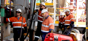 A group of men wearing hard hats and orange jacketsDescription automatically generated