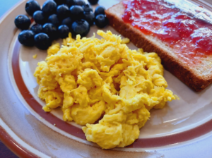A plate of food with blueberries and eggsDescription automatically generated