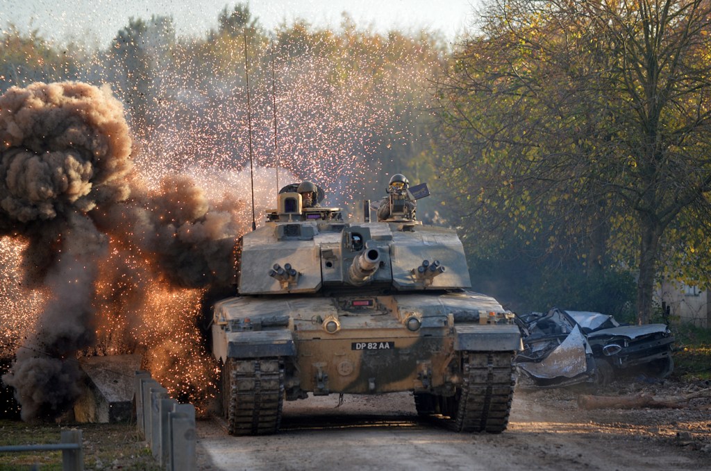 A military tank on a road with smoke and treesDescription automatically generated