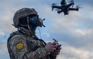 A person in military uniform and helmet holding a droneDescription automatically generated
