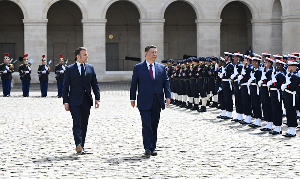 A group of men in suits walking in front of a group of soldiersDescription automatically generated
