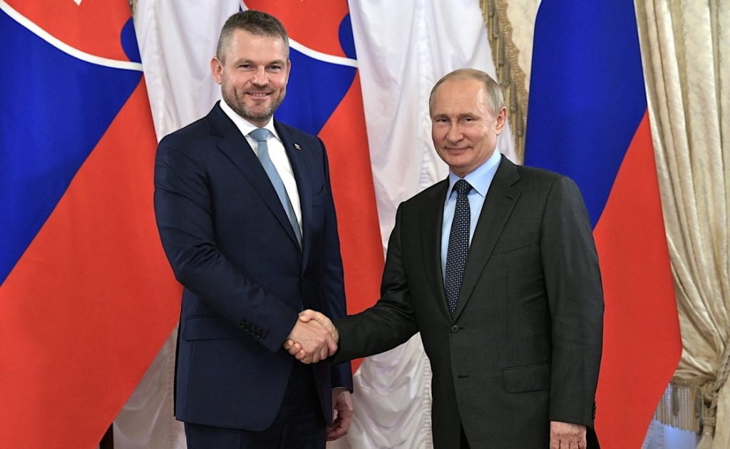 Two men shaking hands in front of flagsDescription automatically generated