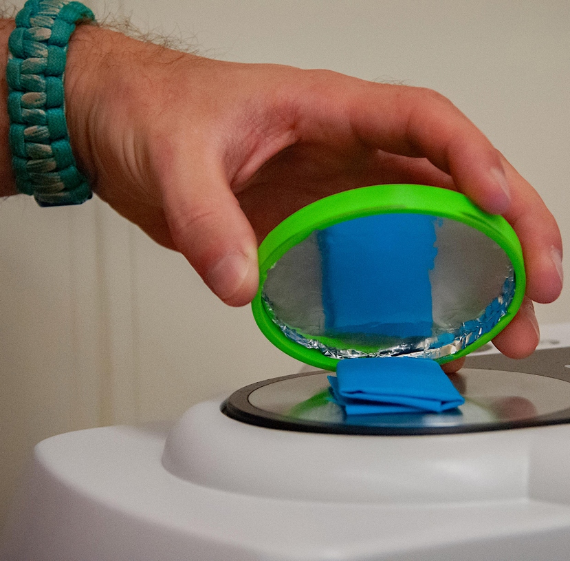 A hand holding a round object over a circular object

Description automatically generated