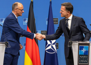 Two men shaking hands in front of flagsDescription automatically generated