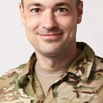 A person in camouflage uniform smilingDescription automatically generated