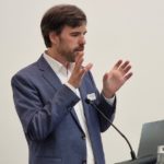 A person standing at a podium with his hands upDescription automatically generated