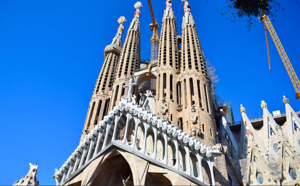 A tall building with towers with Sagrada Família in the backgroundDescription automatically generated