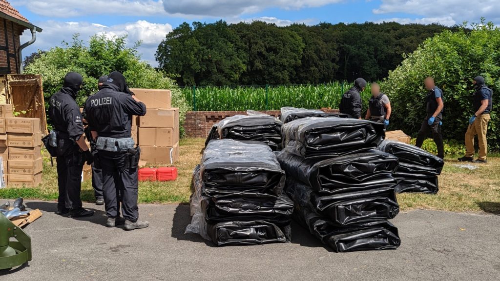 A group of men standing next to a pile of black plastic bagsDescription automatically generated