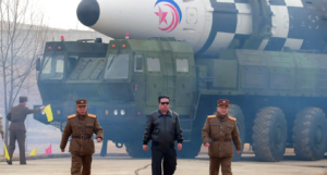 A group of men walking in front of a military vehicleDescription automatically generated