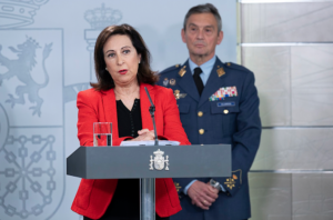 A person standing at a podium with a person in uniform behind herDescription automatically generated