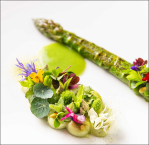 A green asparagus with flowers and green sauce Description automatically generated