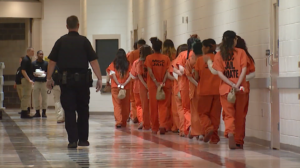 A group of people in orange jumpsuits walking in a hallwayDescription automatically generated