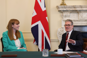A person and person sitting at a table with flagsDescription automatically generated